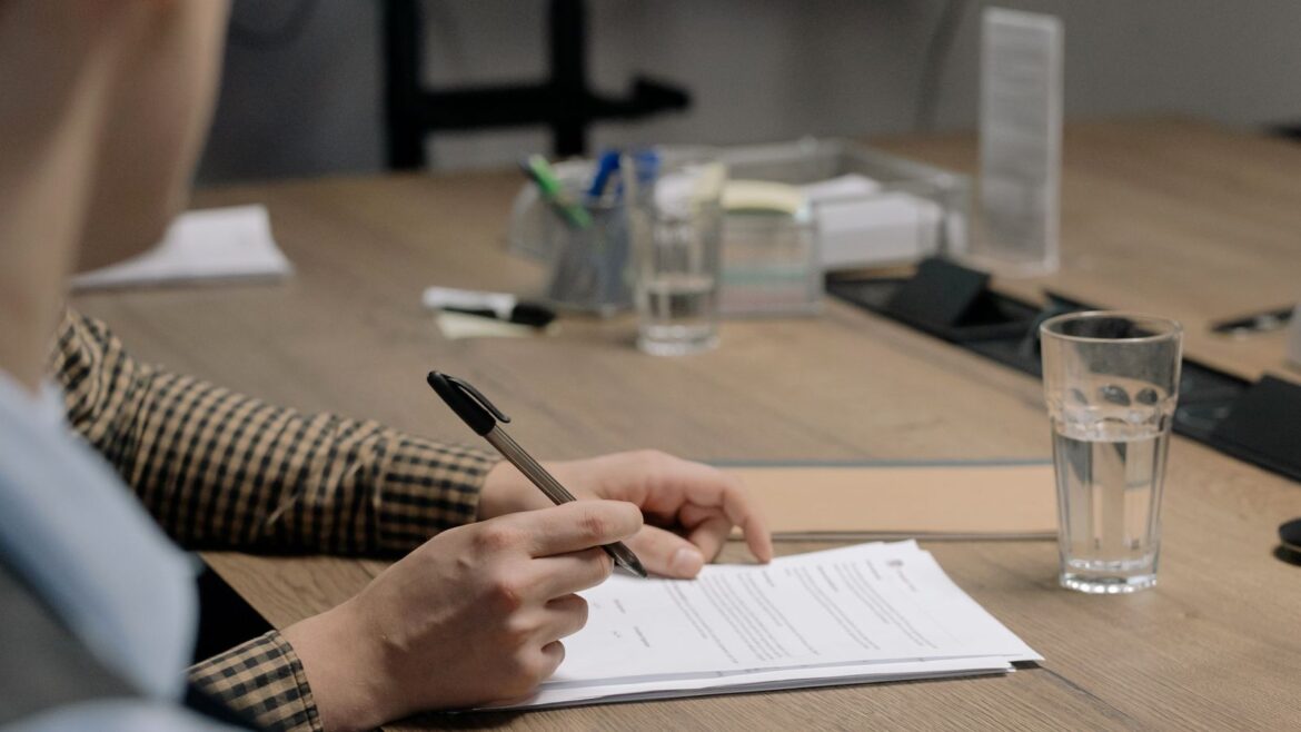 Personne en tenue professionnelle signant un document sur table en bois, bureau