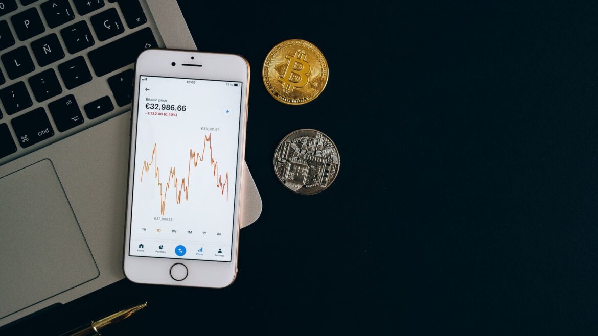 Smartphone affichant un graphique de cours, pièces crypto sur fond noir